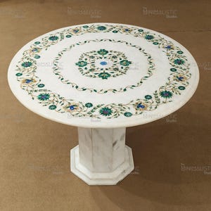 May include: Round white marble table with a decorative floral inlay in green, blue, and white. The table has a pedestal base. The table's diameter is approximately 91 cm.