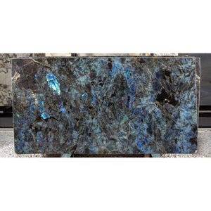 May include: A large rectangular slab of polished granite with a striking pattern of blues, blacks, and greys. The stone features iridescent blue patches and veining, creating a dynamic and textured surface. The granite is displayed on a stand.