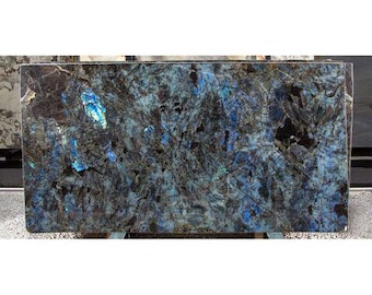 May include: A large rectangular slab of polished granite with a striking pattern of blues, blacks, and grays. The stone features iridescent blue patches and veining, creating a dynamic and textured surface. The granite is displayed on a stand.