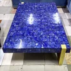 Könnte beinhalten: Ein rechteckiger Couchtisch mit einer blauen Mosaikplatte und goldfarbenen Beinen. Die Tischoberfläche besteht aus kleinen, unregelmäßig geformten Teilen, die ein strukturiertes Aussehen erzeugen. Die Beine sind rechteckig.