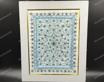 Puede incluir: Obra de arte enmarcada con un diseño floral detallado en tonos azules, verdes y blancos. La obra de arte está enmarcada en un marco blanco con un borde interior dorado. El diseño tiene un patrón central en forma de estrella.