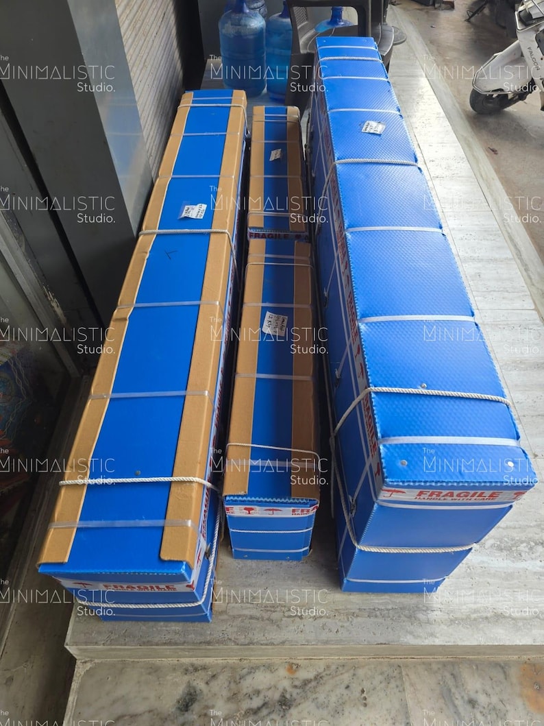 May include: Three rectangular packages wrapped in blue and brown cardboard, secured with white rope. The packages are labeled with the text "FRAGILE" and "The MINIMALISTIC Studio."