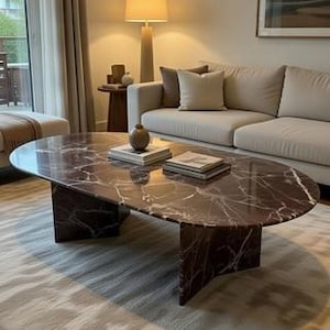 Peut inclure: Table basse ovale en marbre brun foncé avec une base géométrique. La table est dans un salon avec un canapé beige, une lampe et un tapis. La table mesure environ 152 cm de long.
