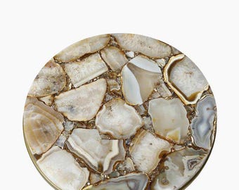 May include: A round side table with a mosaic top made of irregularly shaped, polished agate stones in shades of white, beige, and brown. The stones are set in a gold-colored metal frame and supported by a gold-colored metal base.