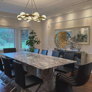 Pode incluir: Uma sala de jantar com uma mesa com tampo de mármore e cadeiras pretas. Um lustre dourado ilumina o espaço. Um grande espelho e obras de arte decorativas adornam a parede. A sala tem janelas grandes e um esquema de cores neutras.