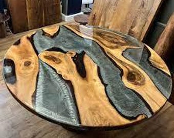 May include: A round table featuring a natural wood slab with prominent knots and grain patterns, integrated with a translucent, smoky gray epoxy resin river flowing through the center. The surface is polished to a high-gloss, smooth finish.
