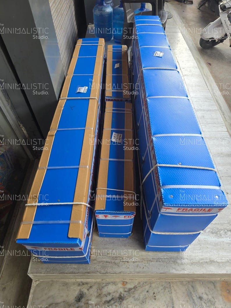 May include: Three rectangular packages wrapped in blue and brown cardboard, secured with white rope. The packages are labeled with the text "FRAGILE" and "The MINIMALISTIC Studio."