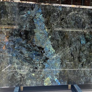 May include: Large slab of polished granite with a dark, textured surface. The stone features a complex pattern of grey, black, and blue veining, creating a dramatic and unique appearance. Ideal for countertops or other design projects.