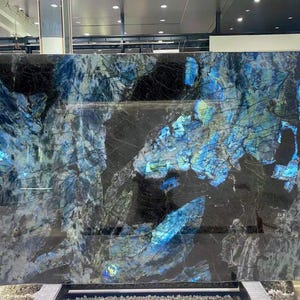 Könnte beinhalten: Große rechteckige Platte aus poliertem Stein mit dunklem Hintergrund und auffälligen blauen und türkisfarbenen Adern. Die Oberfläche des Steins reflektiert das Licht und erzeugt einen schimmernden Effekt. Ideal für Arbeitsplatten oder Dekorplatten.