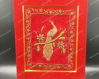 Puede incluir: Una caja de terciopelo rojo con un diseño de pavo real bordado con marco dorado. El pavo real está posado en una rama con detalles azules y florales dorados. La caja tiene un borde dorado.