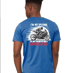 May include: A royal blue t-shirt with a white graphic of a person riding a motorcycle. The text on the shirt reads "I'm not speeding, I'm just testing my bike's capabilities."