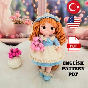 Könnte beinhalten: Eine handgefertigte Häkelpuppe mit roten Locken, die ein blaues und cremefarbenes Kleid trägt und rosa Rosen hält. Die Puppe hat eine blaue Haube und passende Schuhe. Der Text "ENGLISH PATTERN PDF" ist enthalten.