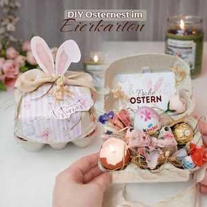 May include: An Easter gift set presented in a repurposed egg carton, adorned with a bunny ear decoration, ribbons, and a tag reading "Osternest". The carton contains sweets, a Kinder egg, and a candle, creating a festive display.