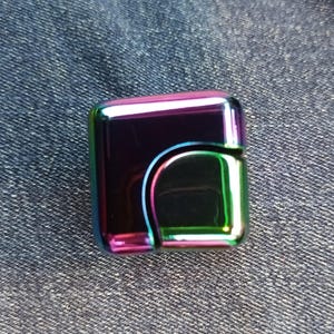May include: A small, rectangular, iridescent lighter with a black interior. The lighter has a green, purple, and pink color scheme.