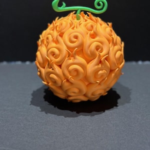 Könnte beinhalten: Ein 3D-gedrucktes orangefarbenes und grünes Modell des Mera Mera no Mi, einer Teufelsfrucht aus dem Anime One Piece.