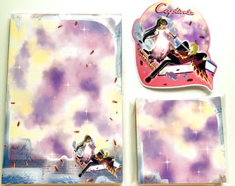 May include: Stationery set featuring a fantasy-themed design with a celestial background in shades of purple, yellow, and white. The set includes a large sheet, a smaller square sheet, and a die-cut sticker with the word "Capitaine".