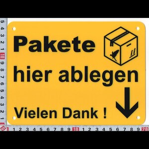 Könnte beinhalten: Gelbes rechteckiges Schild mit schwarzem Text: "Pakete hier ablegen Vielen Dank!" Ein schwarzer Pfeil zeigt nach unten. Eine Grafik einer Box mit Vogel und Pfeilen nach oben befindet sich oben rechts. Das Schild hat vorgebohrte Löcher.