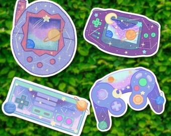 May include: Four colorful stickers featuring retro video game consoles with a space theme. The stickers feature a purple Game Boy Color, a blue Nintendo 64 controller, a purple Game Boy Advance, and a pink Tamagotchi.