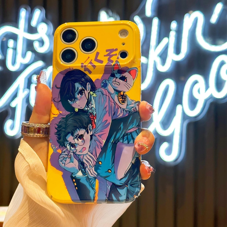 May include: Yellow phone case featuring an anime-style illustration of two people and a cat. The case has a glossy finish and a design with blue, pink, and white accents. The case has a camera cutout and button covers.