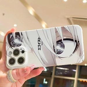Op de afbeelding: Witte telefoonhoes met een manga-stijl illustratie van de ogen en het haar van een personage. Het ontwerp bevat Japanse tekst en een zwart-wit kleurenschema. De hoes heeft een camera-uitsparing en wordt in een hand gehouden.