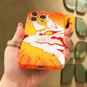 K&ouml;nnte beinhalten: Orange-gelbes Handycase mit einer wei&szlig;en und roten Illustration eines knurrenden Wolfes. Das Case hat eine gl&auml;nzende Oberfl&auml;che und wird in einer Hand gehalten.
