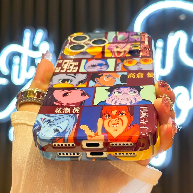 May include: A colorful phone case featuring a manga-style design with various panels of illustrations. The case has a glossy finish and a mix of vibrant colors, including red, blue, yellow, and purple. Japanese text is visible on the case.