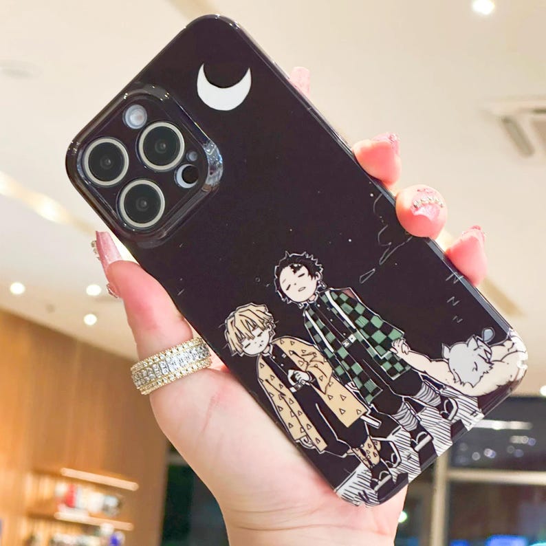 K&ouml;nnte beinhalten: Schwarze Handyh&uuml;lle mit einer Anime-Illustration von drei Charakteren und einem wei&szlig;en Halbmond. Die H&uuml;lle hat eine gl&auml;nzende Oberfl&auml;che und einen Ausschnitt f&uuml;r eine Mehrfachlinsenkamera.