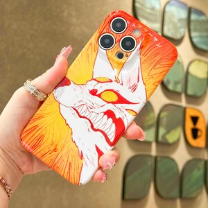 K&ouml;nnte beinhalten: Handyh&uuml;lle mit einer lebendigen Illustration eines wei&szlig;en und roten wolfs&auml;hnlichen Wesens mit gelben Augen vor einem feurigen orange-gelben Hintergrund. Die H&uuml;lle hat drei Kameraausschnitte und japanischen Text.
