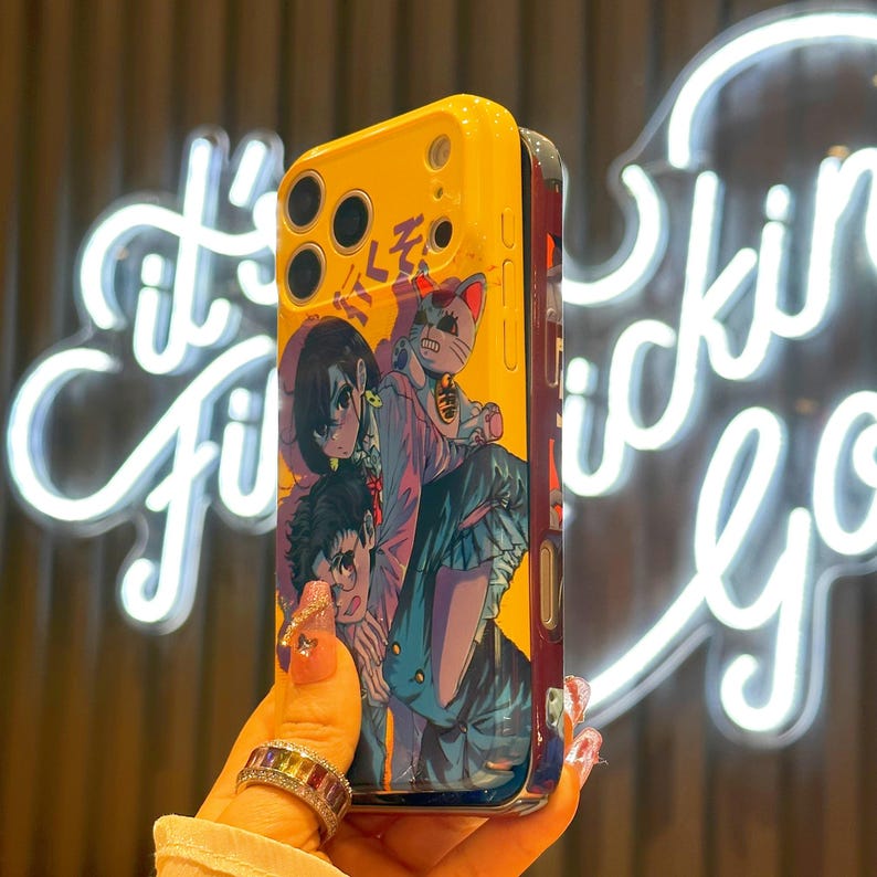 May include: Yellow and blue phone case featuring an anime-style illustration. The case has a glossy finish and a design with multiple characters and a cat. The case has a yellow top with camera cutouts.