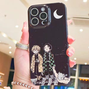 K&ouml;nnte beinhalten: Schwarze Handyh&uuml;lle mit einer Anime-Illustration von zwei Charakteren und einem Halbmond. Die H&uuml;lle hat eine gl&auml;nzende Oberfl&auml;che und einen transparenten Kameraschutz. Das Design umfasst Charaktere in gemusterter Kleidung.
