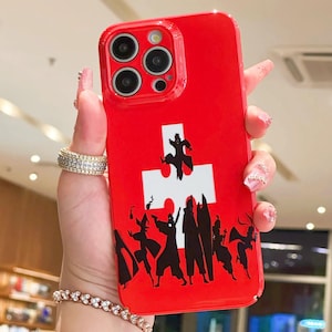 May include: A red phone case featuring a white puzzle piece design with a black silhouette of figures. The case has a glossy finish and a camera cutout.