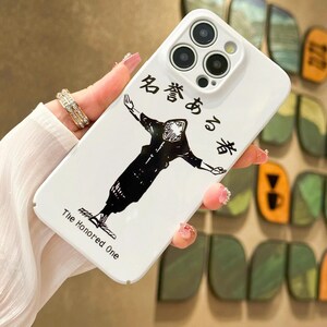 May include: White phone case with a black illustration of a figure with outstretched arms. Japanese text and the English text "The Honored One" are printed on the case. The case has a camera cutout and is held at an angle.