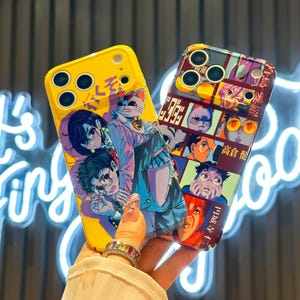 May include: Two phone cases with anime-style illustrations. One is yellow with a manga-style design featuring characters and Japanese text. The other case is a mix of colors with a collage of anime faces and Japanese text. Both cases have a glossy finish.