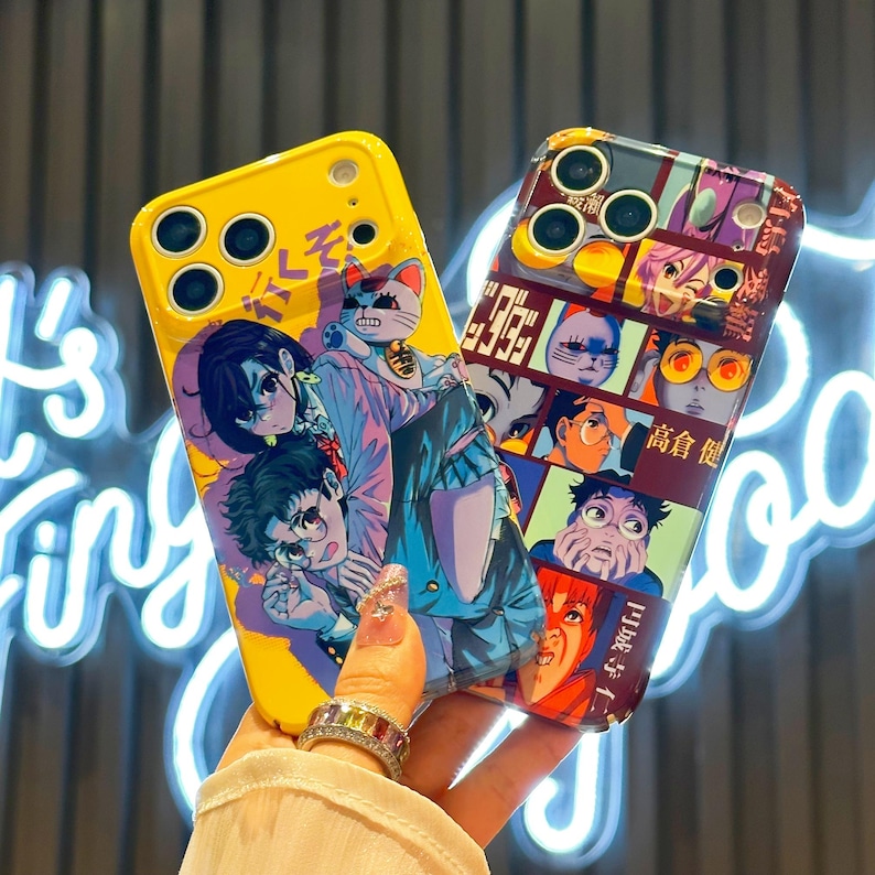 May include: Two phone cases with anime-style illustrations. One is yellow with a manga-style design featuring characters and Japanese text. The other case is a mix of colors with a collage of anime faces and Japanese text. Both cases have a glossy finish.