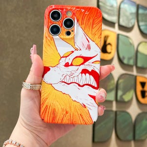 May include: A phone case featuring a white and red wolf illustration with sharp teeth against a yellow and orange background. The case has a glossy finish and a camera cutout. The design is a stylized, cartoon-like image.
