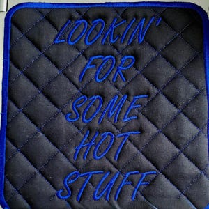 Könnte beinhalten: Schwarzer, gesteppter Untersetzer aus Stoff mit blauer Stickerei, auf der "Lookin' for some hot stuff" steht.