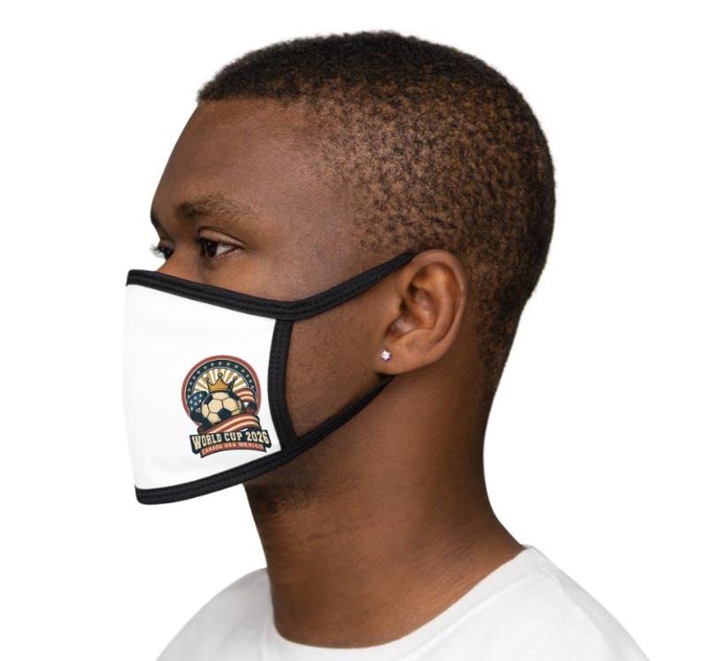 May include: White face mask with black trim featuring a soccer ball design, a crown, and the text "WORLD CUP 2026 CANADA USA MEXICO". The mask is worn by a person.