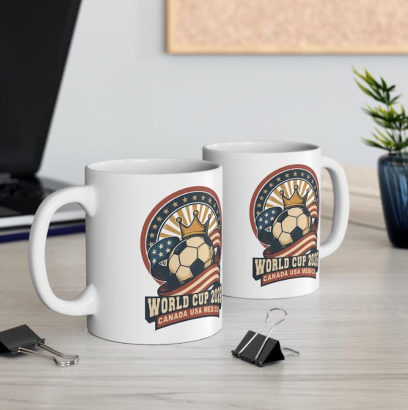 May include: Two white ceramic mugs with a soccer-themed design. The design features a soccer ball with a crown, surrounded by a red, white, and blue circular emblem with the text "WORLD CUP 2026 CANADA USA MEXICO".