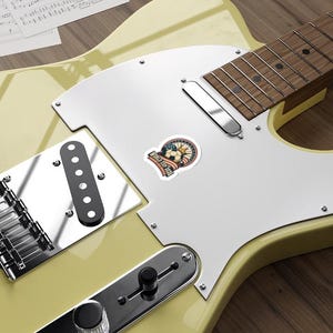 May include: A sticker with a soccer ball design, featuring the text "World Cup 2026". The sticker has a vintage aesthetic with red, white, and blue colors, and is placed on a light yellow electric guitar.