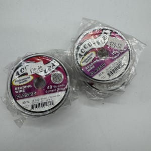 Pode incluir: Dois rolos de fio para miçangas, ambos etiquetados como "Accu-Flex Professional Quality Beading Wire Classic". O rolo à esquerda custa $ 20,00 e o rolo à direita $ 26,50. Ambos os rolos têm 9,1 metros de comprimento e são feitos no Japão.