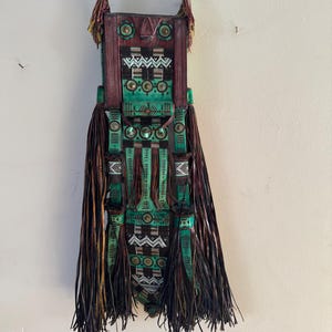 May include: A green and brown leather bag with intricate geometric patterns and fringe. The bag has a long strap and is decorated with metal accents.