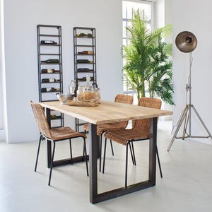 Könnte beinhalten: Ein Esstisch aus Holz mit einem schwarzen Metallgestell und vier Korbstühlen. Zwei schwarze Metallweinregale befinden sich an der Wand hinter dem Tisch.