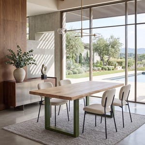 Può includere: Un set da pranzo composto da un tavolo rettangolare in legno chiaro con gambe in metallo a forma di U color verde oliva, accompagnato da quattro sedie imbottite color crema con sottili telai in metallo nero, su un tappeto grigio.