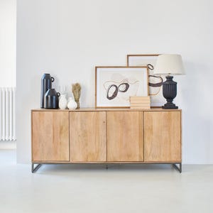 Könnte beinhalten: Ein helles Holzschrank mit vier Türen vor einer weißen Wand. Der Schrank ist mit dekorativen Gegenständen wie schwarzen Vasen, gerahmter Kunst und einer schwarzen Lampe mit beigem Schirm versehen. Der Schrank steht auf einem Metallrahmen. Ca. 150 cm lang.