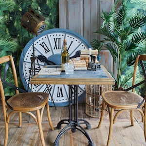 Puede incluir: Escena interior de estilo vintage con un gran reloj con números romanos, una mesa pequeña y dos sillas de madera. La mesa tiene una base de metal y una tapa de piedra. Una botella, vasos y libros están sobre la mesa.