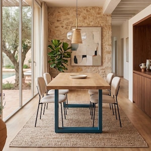Può includere: Un tavolo da pranzo rettangolare in legno con un piano spesso e gambe in metallo blu a forma di U, circondato da quattro sedie imbottite color bianco sporco con telai in metallo nero. Una singola ciotola bassa poggia al centro del tavolo.