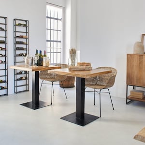 Puede incluir: Dos mesas cuadradas de madera con patas de metal negro y sillas de mimbre tejido. Las mesas están preparadas con vasos, botellas y una cesta de artículos decorativos. Las mesas están en una habitación blanca con una ventana grande y un armario de madera.