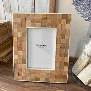 Op de afbeelding: Een houten fotolijst met een witte rand en een mozaïek van kleine houten vierkanten. De lijst heeft een witte passe-partout en een heldere glazen voorkant. De lijst is gemaakt door het bedrijf "Orchidéa Milano 1981".