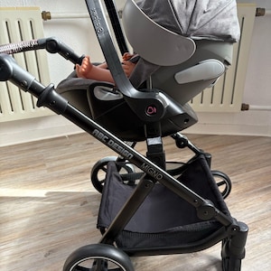Puede incluir: Un cochecito negro y gris con el texto "ABC DESIGN MIGNO" y "cybex". El cochecito tiene un asiento de coche para bebés gris adjunto. Las ruedas son negras con un borde plateado. El cochecito tiene una cesta de almacenamiento negra debajo.