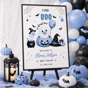 Może przedstawiać: Prostokątny znak w czarnej ramce z napisem A little BOO is almost due! Welcome to Elena's Wilson Baby Shower 23 | June | 2028. Projekt zawiera ducha w niebieskiej dyni, kapelusz czarownicy, kociołek oraz nietoperze w kolorach niebieskim i czarnym.
